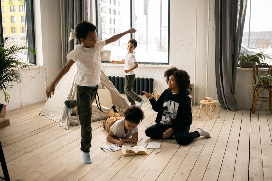 A home childcare provider sits on the floor playing with a small group of children in a bright, cozy room